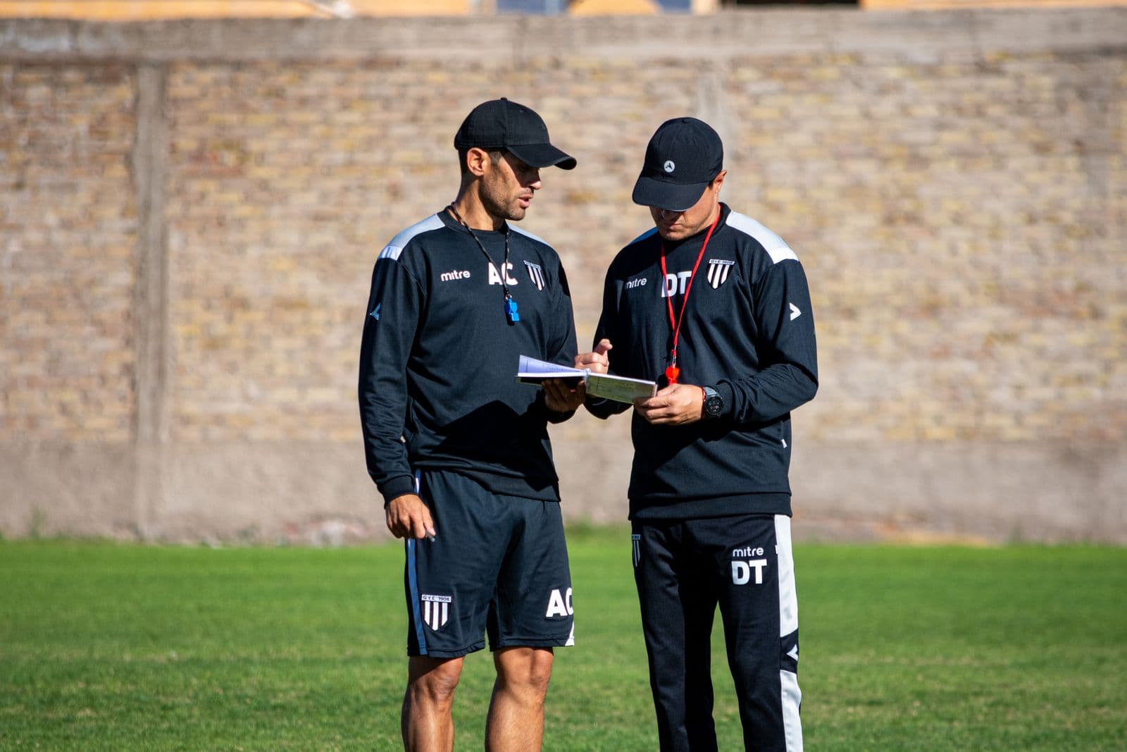 El cuerpo técnico repasando la planilla del partido al borde de la cancha